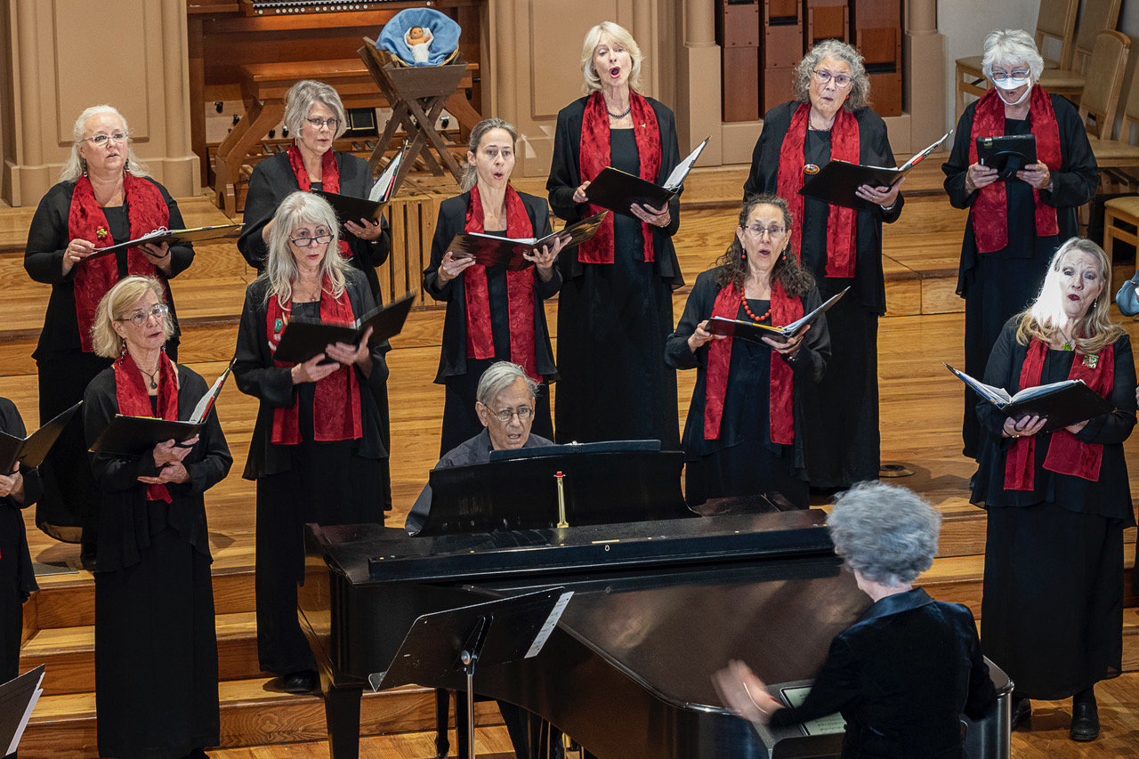 Singers in black with red scarves, singing on stage