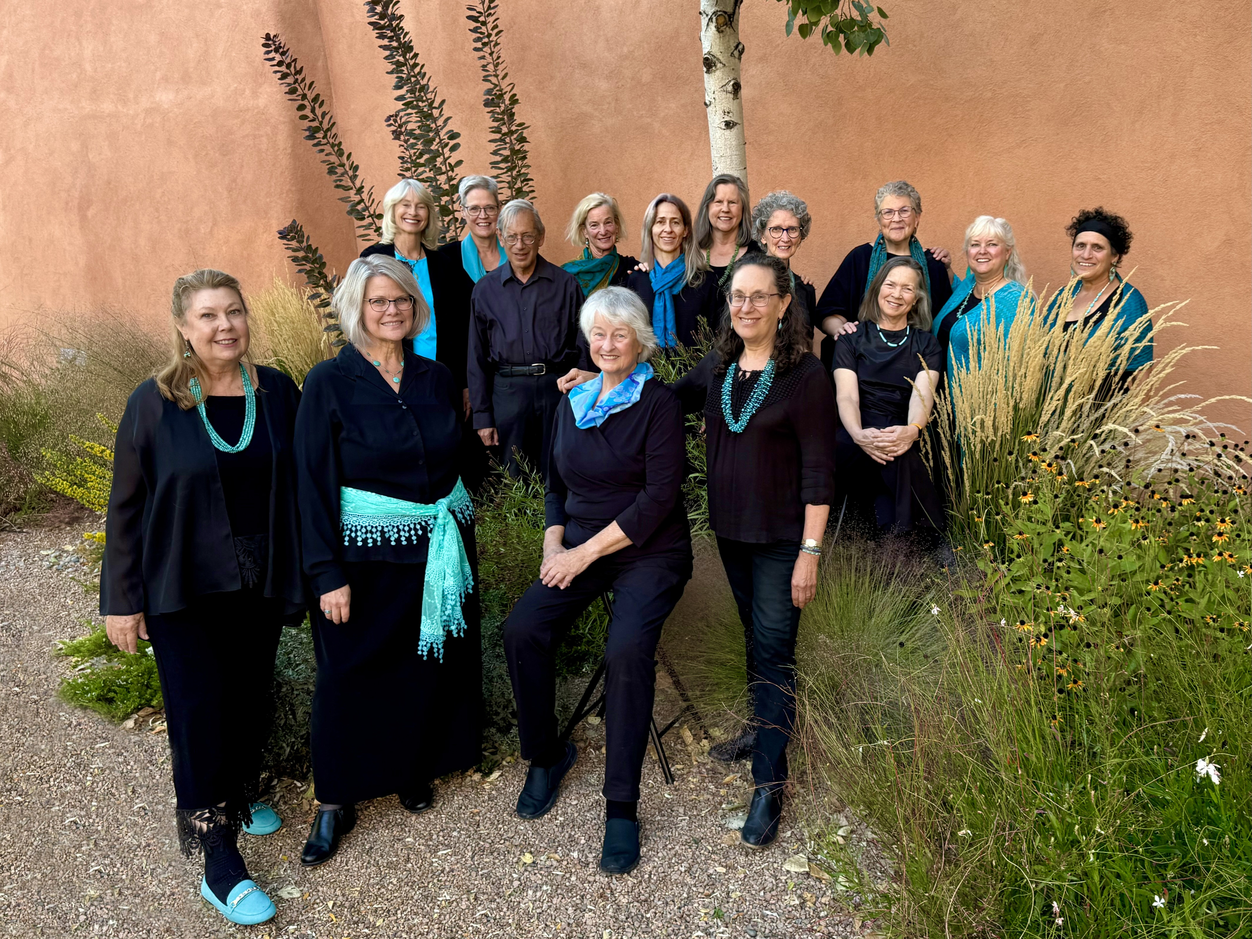 group of smiling people wearing black with turquoise accents, standing in garden setting